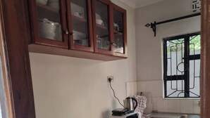 A compact kitchen with a refrigerator, microwave, and a wooden shelf with pots. - Voyage Camp Safari Lodge (Arusha)