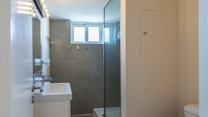 Moderni kylpyhuone, jossa on lasinen suihkuseinä, valkoinen pesuallas ja wc-istuin.