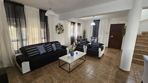 A living room with a black sofa, a white coffee table, and a blue vase. There is a staircase to the right and a door at the top. - 124 PRO 1 - Stay Villa Prince (Paralimni)