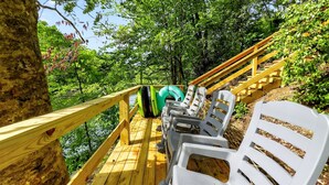 Une terrasse en bois avec des chaises en plastique et un grand cercle gonflable vert, le tout entouré d’une végétation luxuriante.