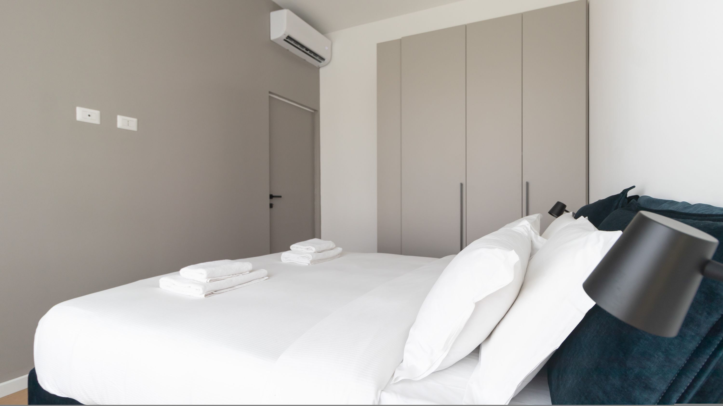 Ein modernes Schlafzimmer mit einem Bett, weißen Bettwäsche, einer dunkelblauen Decke und einer schwarzen Lampe.