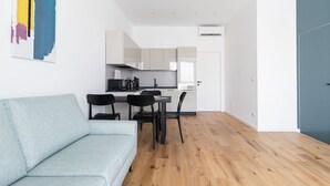 A modern living room with a light blue sofa, a dining area with a black table and chairs, and a kitchen with white cabinets and a black countertop. - Italianway Comfort - D Aragona 2 (Milan)