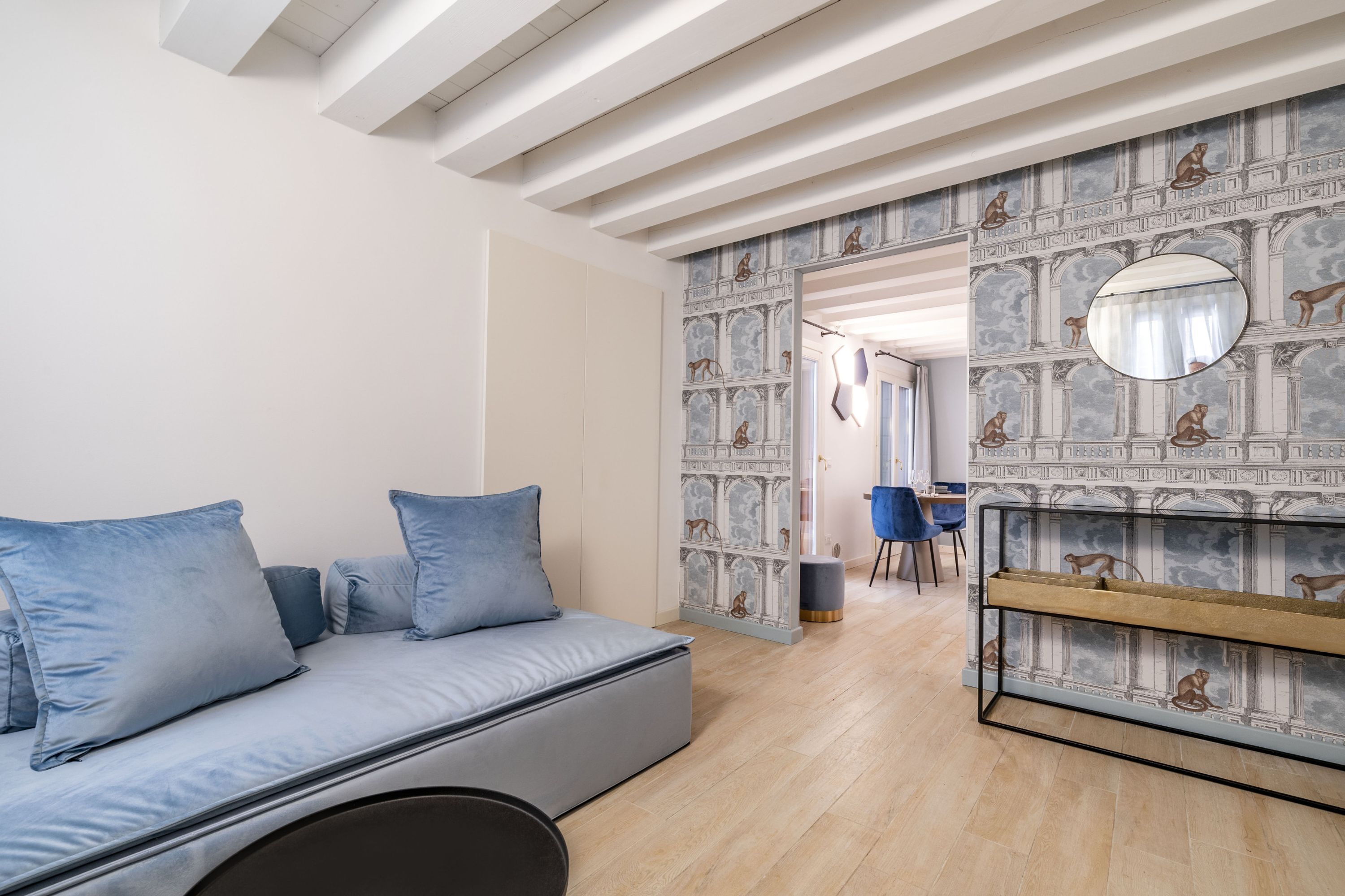 Une pièce moderne avec un canapé, un miroir rond et un mur orné d’un motif.
