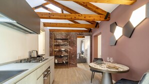 Una cocina moderna con estufa integrada, una zona de comedor con una mesa redonda y dos sillas, y techo de madera.