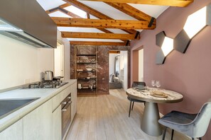 Una cocina moderna con estufa integrada, una zona de comedor con una mesa redonda y dos sillas, y techo de madera.