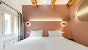 Una habitación de hotel con una cama grande, dos mesitas de noche, una lámpara fijada a la pared y una ventana con cortinas.