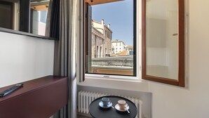 Una habitación con vistas a edificios a través de una ventana, una mesa con dos tazas y un control remoto sobre un banco.