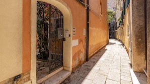 A narrow cobblestone alley with a building featuring an arched entrance and a metal gate. - The Green Jungle by Wonderful Italy (Venice)