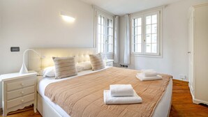 A bedroom with a large bed, white nightstands, a bedside lamp, and a window with curtains. - Tolentini Terrace - Locz (Venice)
