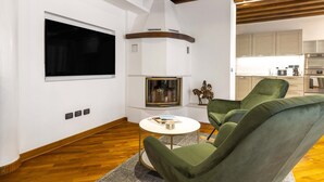 A modern living room with a fireplace, green armchairs, a round coffee table, and a kitchen in the background. - Tolentini Terrace - Locz (Venice)