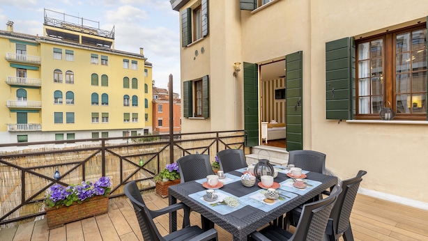 A terrace with a table set for dining, surrounded by wicker chairs, and overlooking a cityscape. - Tolentini Terrace - Locz (Venice)