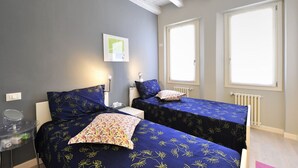 Une chambre avec deux lits, chacun recouvert d’une couette à motifs floraux, une table de chevet avec un miroir et une fenêtre donnant sur un paysage agréable.