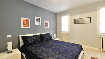 A bedroom with a bed, bedside tables, artwork on the wall, a window, and a radiator.