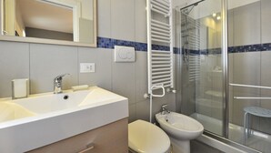 Une salle de bain moderne avec un grand lavabo blanc, un bidet, une douche en verre et un porte-serviettes.