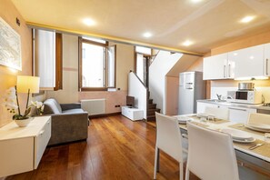A modern kitchen with white cabinets, a dining area with a table set for two, and a staircase leading to an upper floor.