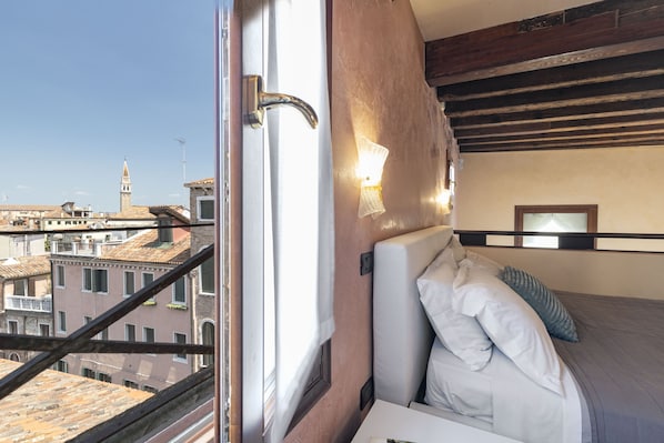 A hotel room with a bed, a window with a view of buildings, and a wooden ceiling.