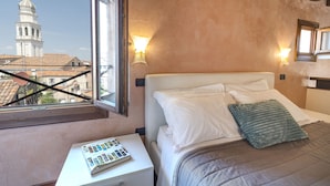 A hotel room with a bed, bedside lamps, a nightstand, and a window with a view of a building. - Doge Palace 8 - Locz (Venice)