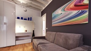 Una sala de estar moderna con un sofá gris, un mueble blanco con recipientes azules y un cuadro abstracto colorido en la pared.