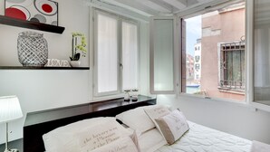 A hotel room with a bed, a bedside table with a lamp, a decorative vase, and a view of the outside. - Marco Polo Apartment by Wonderful Italy (Venice)