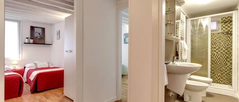 Una habitación con dos camas, suelo de madera, baño con ducha e inodoro.