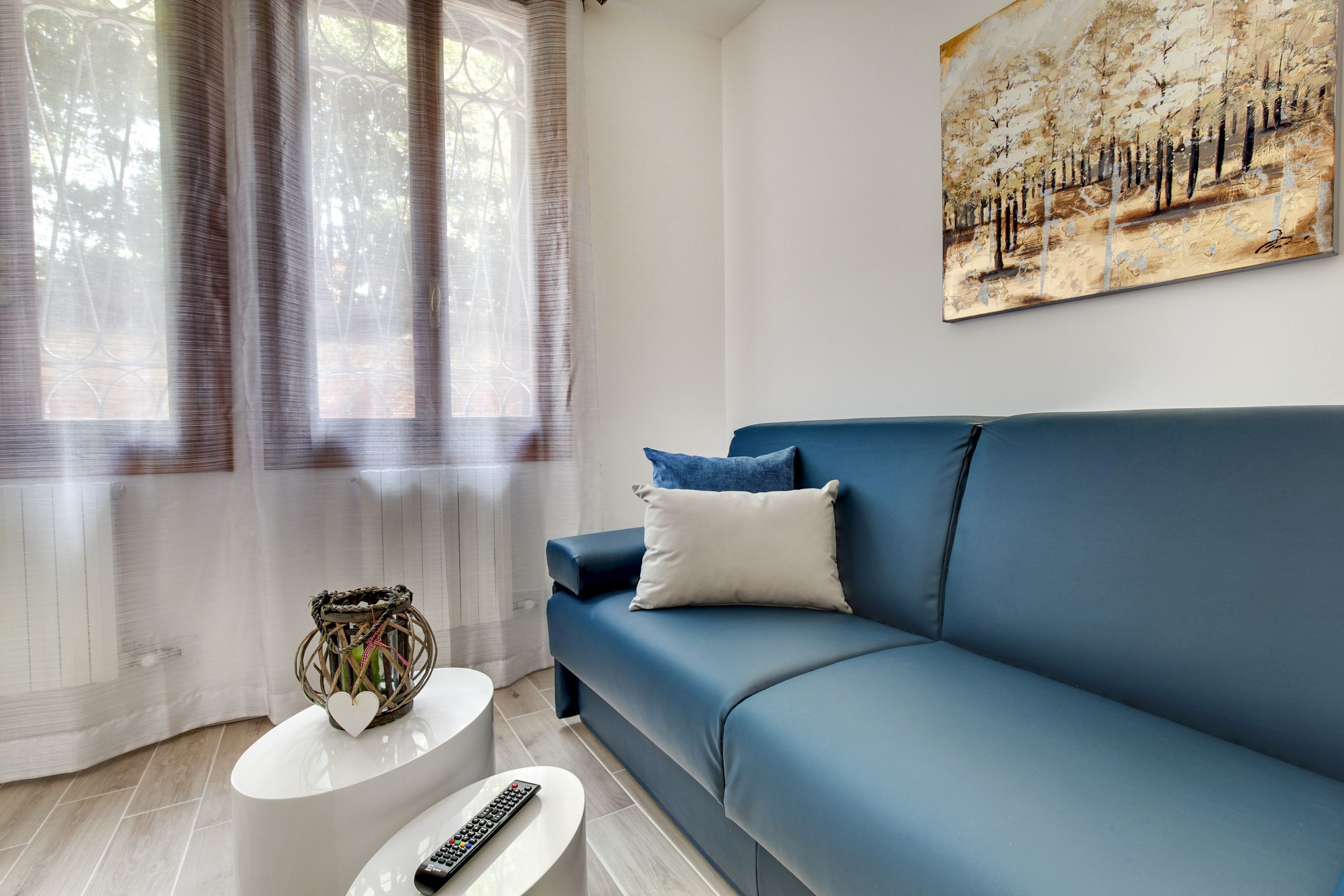 A modern living room with a blue sofa, white coffee table, and a painting on the wall.