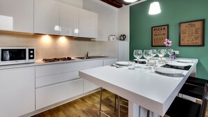 Une cuisine moderne avec des meubles blancs, un four à micro-ondes, une cuisinière à gaz et un coin repas aménagé pour quatre personnes, avec des verres et des assiettes.