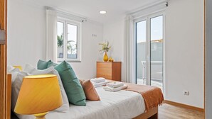 Un dormitorio moderno con cama, lámpara de noche, cómoda y ventana con vistas.