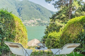 Eine Terrasse mit zwei Stühlen und einem Tisch mit Blick auf einen See, vor dem sich Berge erheben.