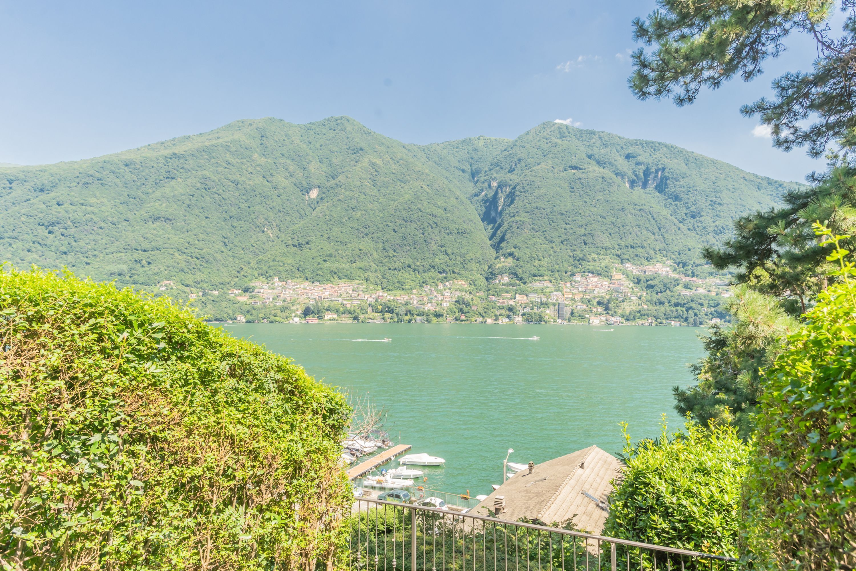 A view of a lake with boats docked at a pier, surrounded by lush green hills and a clear sky.