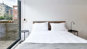 A modern hotel room with a large bed, a small round table, a nightstand with a lamp, and a view of the city through a large window. - w Radiant Loft w Amazing Terrace in Bogota (Bogotá)