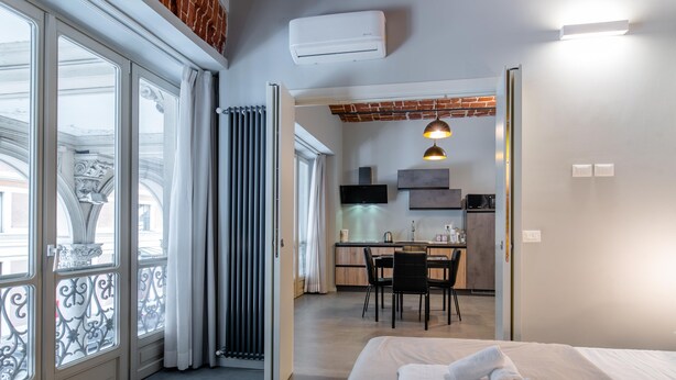 A modern hotel room with a large bed, a dining area, and a kitchen in the background. - Queen Apartment in Torino (Turin)