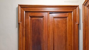 A wooden double door with a brass handle and a keyhole, set in a hallway with a light-colored wall and a marble floor. - Queen Apartment in Torino (Turin)