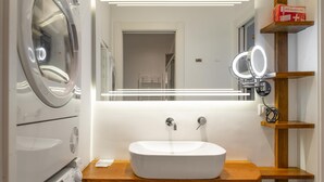 A modern bathroom with a built-in washing machine, a sink with a wooden countertop, and a mirror with lights. - Queen Apartment in Torino (Turin)