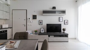 A modern living room with a flat-screen TV, a coffee table, and a dining area with a table and chairs. - Italianway Comfort - Fara 29 (Milan)