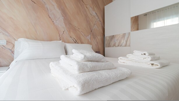 A hotel room with a marble-patterned headboard, a neatly made bed with white linens, and a stack of folded towels. - Italianway Comfort - Fara 29 (Milan)