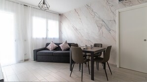 A modern living room with a dark sofa, two patterned cushions, a dining table with chairs, and a marble wall. - Italianway Comfort - Fara 29 (Milan)