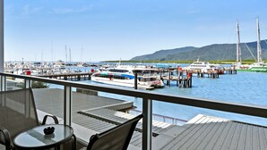 Un balcón con mesa y sillas de vidrio que da a un puerto deportivo con barcos y un muelle.