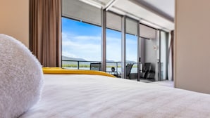 Habitación de hotel con cama, vistas al exterior y balcón con sillas.