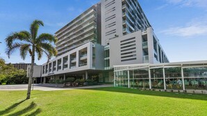 Un hotel moderno de varios pisos con un atrio central, zona de estar al aire libre y una palmera en primer plano.