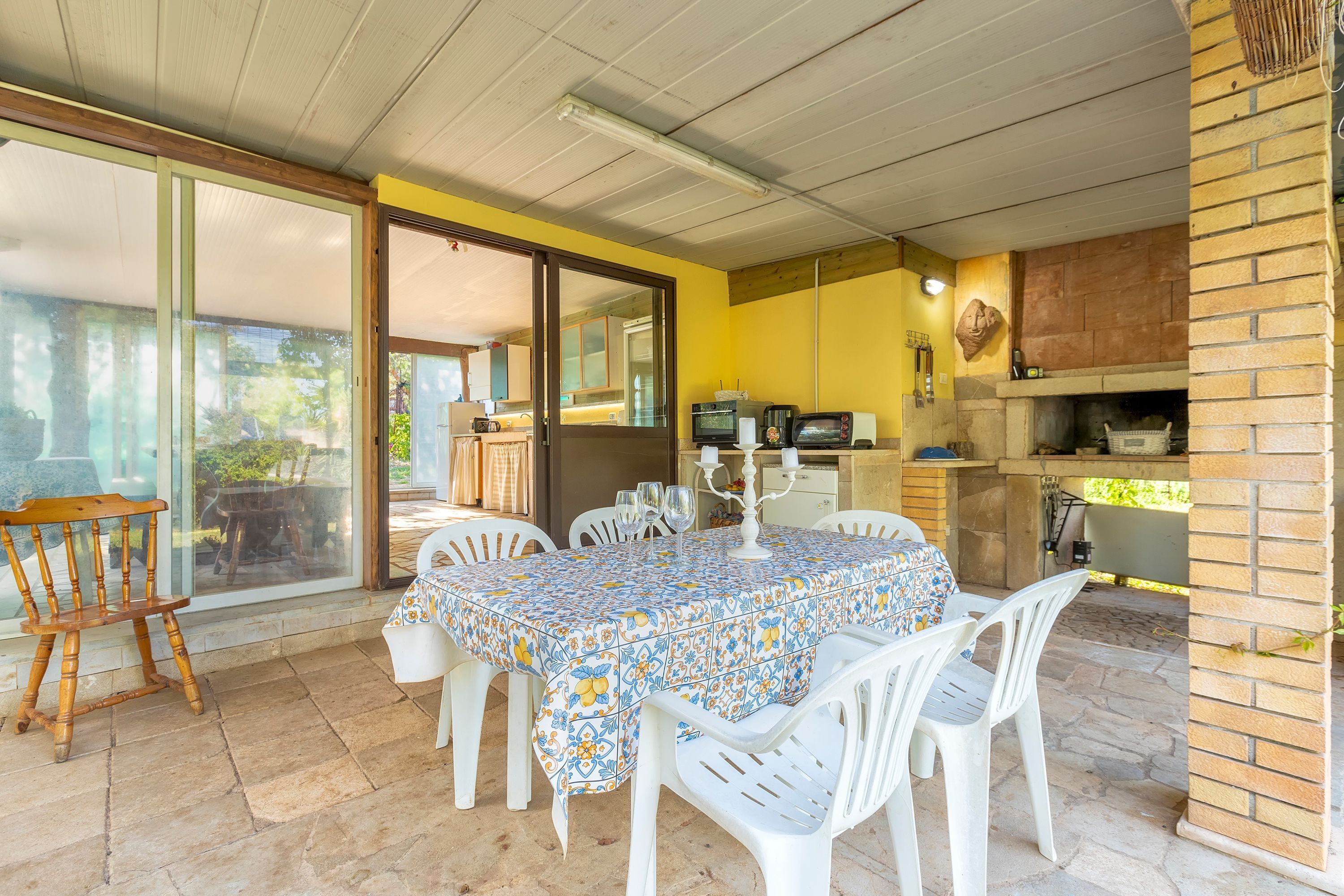 A dining area with a table covered by a patterned tablecloth, surrounded by white plastic chairs.