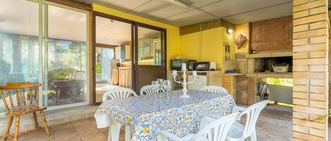 A dining area with a table covered by a patterned tablecloth, surrounded by white plastic chairs.