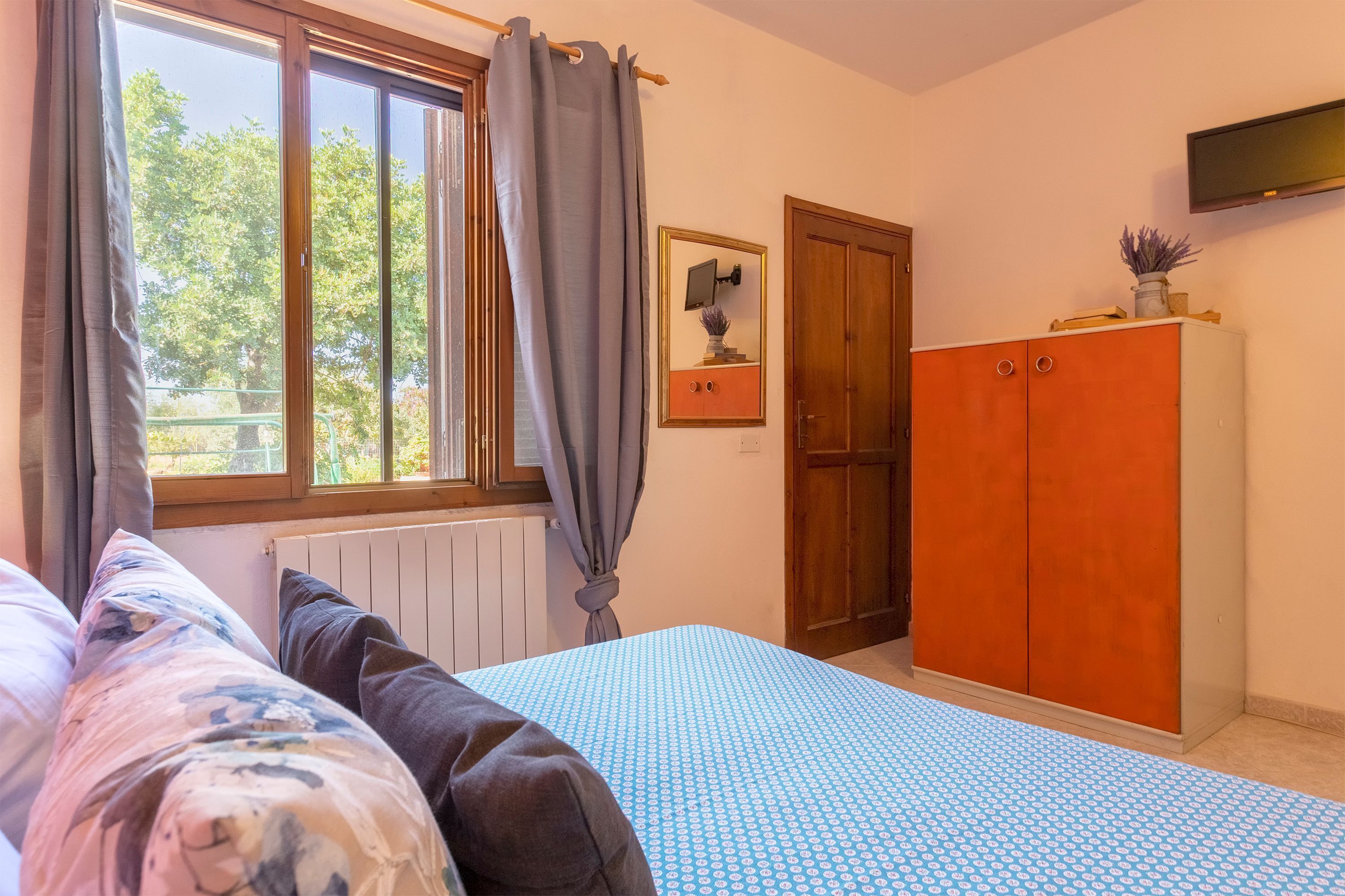 A bedroom with a bed, a window with curtains, a wardrobe, and a framed picture on the wall.