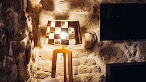 A stone wall with a wooden chair and a table lamp.