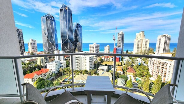 Varanda com mesa e cadeiras, vista para um horizonte urbano com edifícios modernos e céu claro.