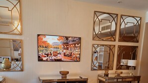 Quarto de hotel com uma grande janela, uma cama, uma escrivaninha, uma cadeira e uma televisão exibindo uma vista panorâmica.