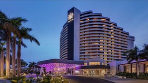 Um hotel moderno com fachada curva, vários andares e um logotipo iluminado em destaque na lateral.