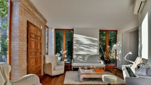 Una sala de estar moderna con un piano, un sofá, un sillón y un ventanal con vistas a zonas verdes.