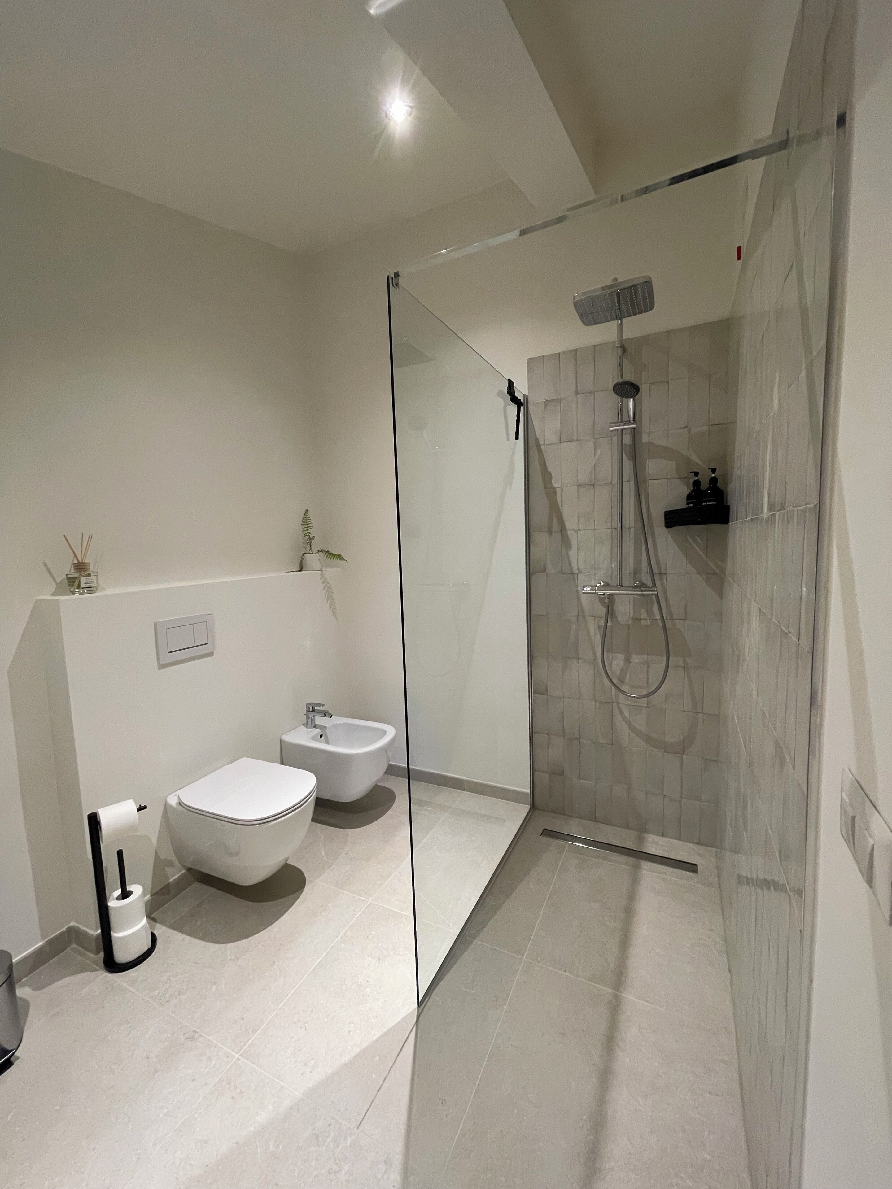 A modern bathroom with a glass-enclosed shower, a bidet, and a toilet.
