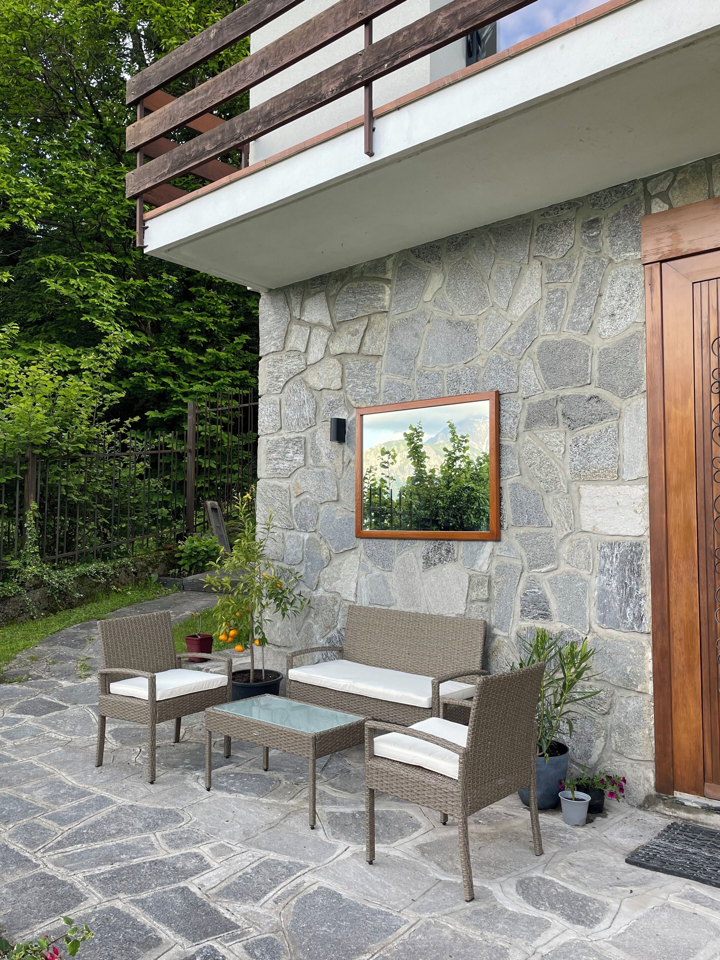 A stone wall with a framed picture, a wooden door, and a balcony with a railing.