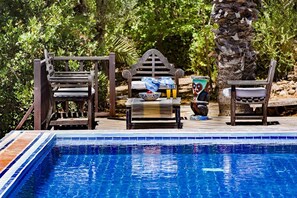 Un espace aménagé au bord de la piscine, avec un banc en bois, une table sur laquelle se trouvent un saladier et des boissons, ainsi qu'un objet décoratif.